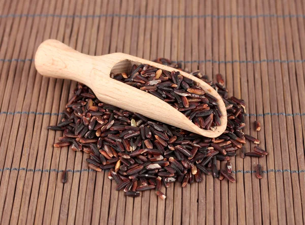 Black rice in wooden scoop on bamboo mat — Stock Photo, Image