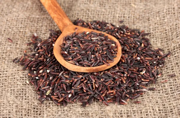 Black rice on sacking in wooden spoon — Stock Photo, Image