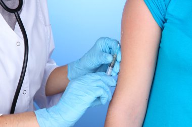 doctor holding syringe with vaccine into patient's shoulder on blue background clipart