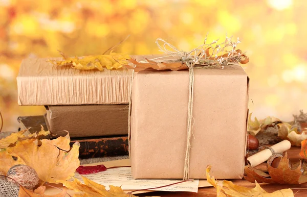 Autumnal composition with gift, books and leaves on bright background