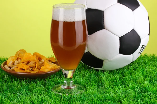 Sklenici piva s fotbalovým míčem na trávě na zeleném pozadí — Stock fotografie