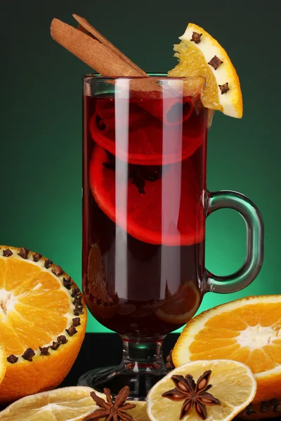 Fragrant mulled wine in glass with spices and oranges around on green background — Stock Photo, Image