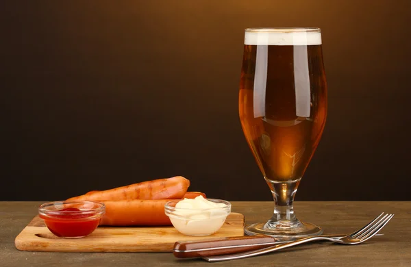 Cerveza y embutidos a la parrilla sobre mesa de madera sobre fondo marrón —  Fotos de Stock