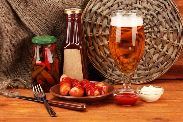 Bière et saucisses grillées sur table en bois sur fond de sac — Photo