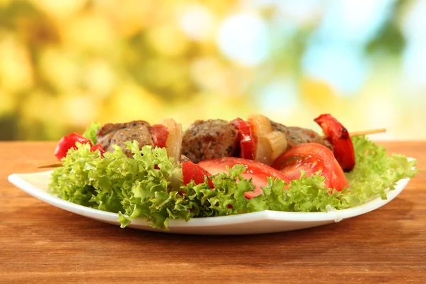 Νόστιμο ψητό κρέας και λαχανικά σε σουβλάκι στο πιάτο, σε ξύλινο τραπέζι — Φωτογραφία Αρχείου