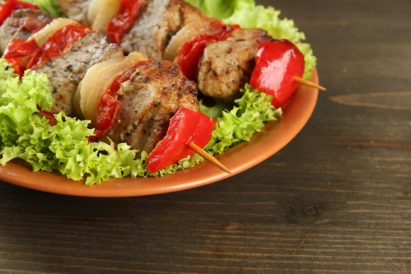 Смачне м'ясо та овочі на шампурі на тарілці, на дерев'яному столі — стокове фото