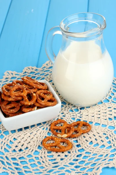 Tasty pretzels in white bowl and milk jug on wooden table close-up — Stock Photo, Image