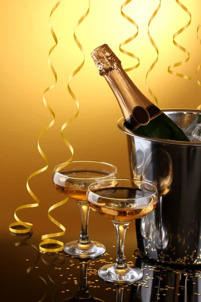 Champagnefles in emmer met ijs en glazen van champagne, op gele achtergrond — Stockfoto