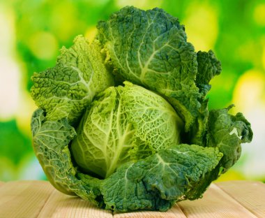 Fresh savoy cabbage on wooden table on natural background