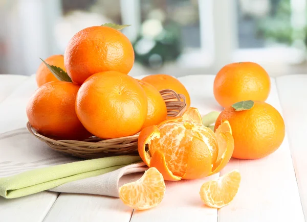 Mandarini con foglie in un bel cesto, su tavolo di legno su fondo finestra — Foto Stock