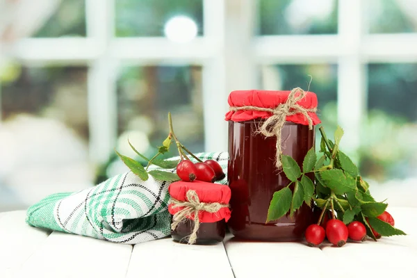 Guci dengan selai mawar pinggul dan buah berry matang, di atas meja kayu — Stok Foto
