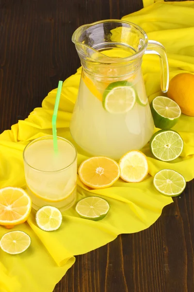 在玻璃和投手的柑橘周围黄色织物上木表特写上柑橘柠檬水 — 图库照片