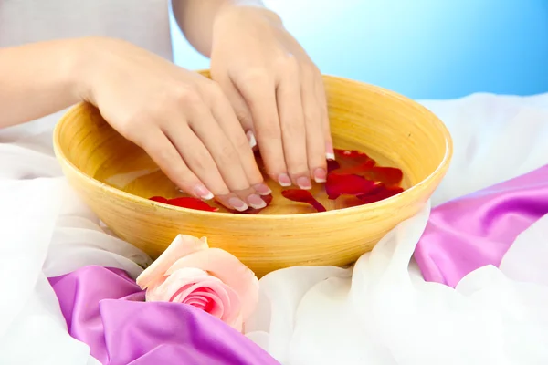 Woman hands with wooden bowl of water with petals, on blue background — Stock Photo, Image