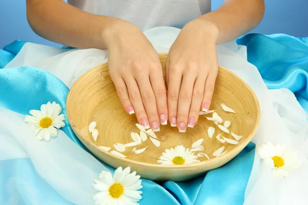 Vrouw handen met houten kom met water met bloemen, op blauwe achtergrond — Stockfoto