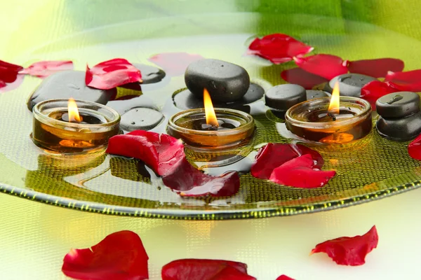 Spa stenen met rozenblaadjes en kaarsen in water op plaat — Stockfoto
