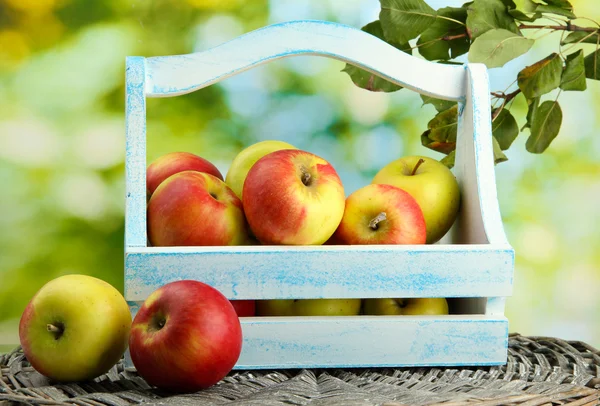 多汁的苹果用叶子在木制的篮子里，绿色背景 — 图库照片