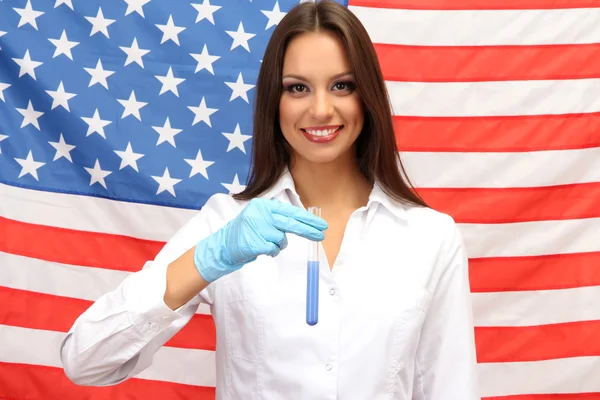 Retrato de doctora o científica mostrando y analizando líquido en frasco sobre fondo de bandera americana — Foto de Stock