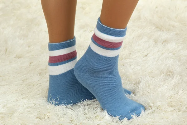 Frauenbeine in bunten Socken auf weißem Teppich-Hintergrund — Stockfoto