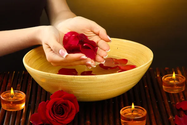 Woman hands with wooden bowl of water with petals, on brown background — Stock Photo, Image