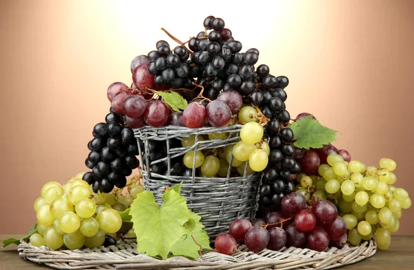 Assortment of ripe sweet grapes in basket, on brown background — Stock Photo, Image