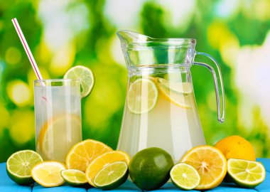 narenciye limonata sürahi ve bardak narenciye çevresinde doğal ahşap masa mavi zemin üzerinde