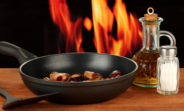 Жареные каштаны в кастрюле и графин с маслом, солью и перцем на деревянном столе крупным планом — стоковое фото