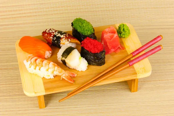 Delicious sushi served on wooden board on bamboo mat — Stock Photo, Image