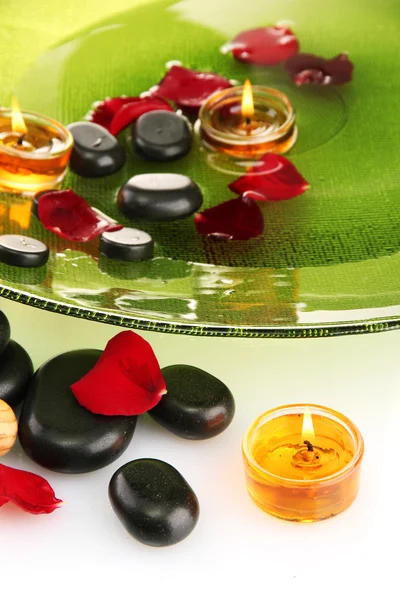 Piedras de spa con pétalos de rosa y velas en agua en placa, aisladas en blanco — Foto de Stock