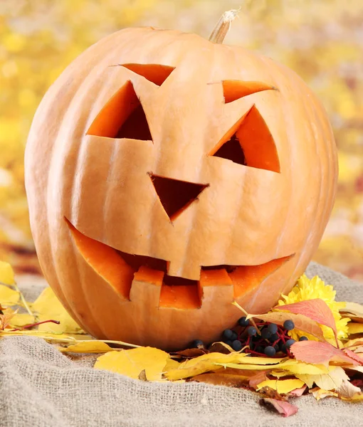 Halloween pumpkin and autumn leaves, on yellow background — Stock Photo, Image