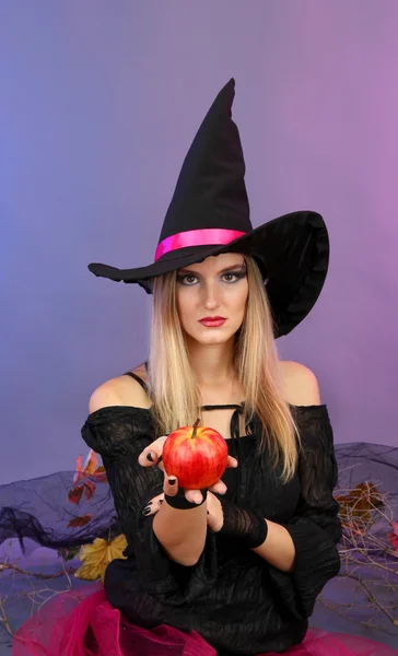 Хэллоуин ведьма с красным яблоком на цветном фоне — стоковое фото