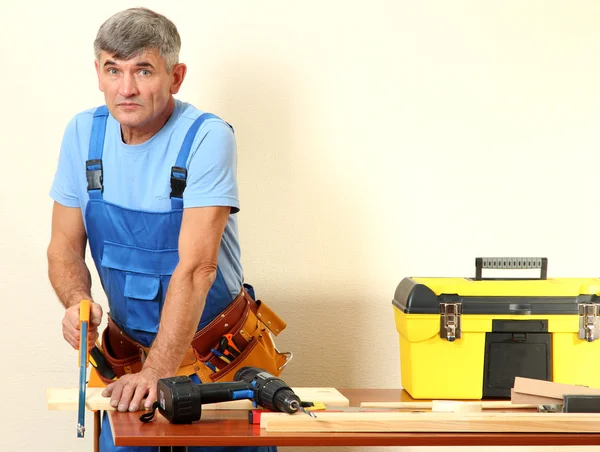 Bauarbeiter sägt Bretter auf Tisch vor Wandhintergrund — Stockfoto