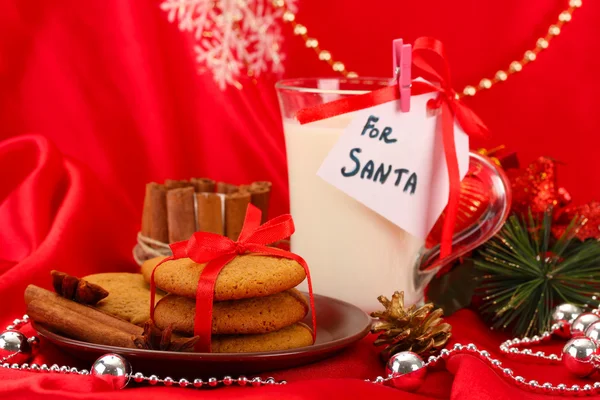 Galletas para Santa: Imagen conceptual de galletas de jengibre, leche y decoración navideña sobre fondo rojo — Foto de Stock