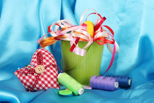 Balde de cor com fitas multicoloridas e linha no fundo de tecido azul — Fotografia de Stock