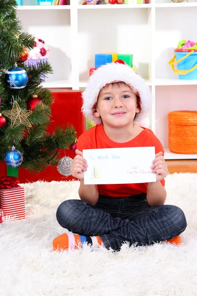 Menino em chapéu de Papai Noel escreve carta para Papai Noel — Fotografia de Stock