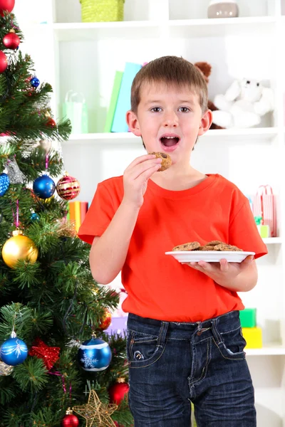 Kleine jongen in de buurt van kerstboom eet cookies — Stockfoto