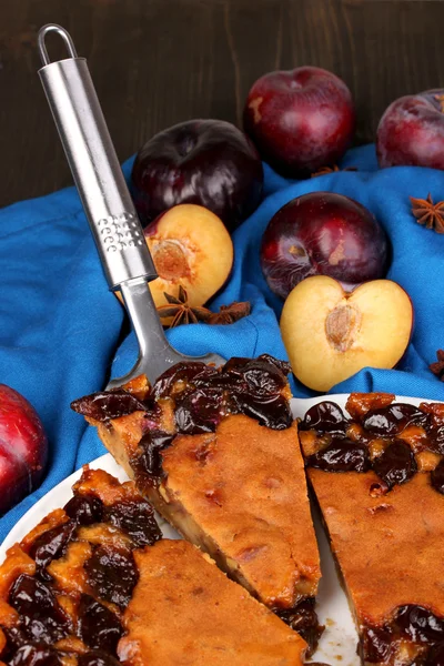 Tasty pie on plate with plums on wooden table — Stock Photo, Image