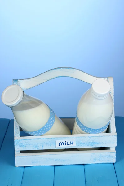 Mleko w butelkach w drewniane pudełko na niebieskim drewnianym stole na niebieskim tle — Zdjęcie stockowe