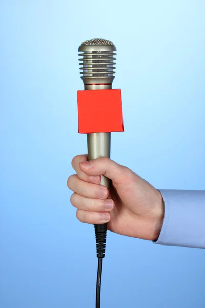 Männliche Hand mit Mikrofon auf blauem Hintergrund — Stockfoto