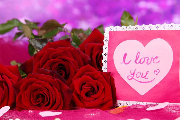 Mooi boeket rozen met valentine op roze stof op paarse achtergrond close-up Stockfoto