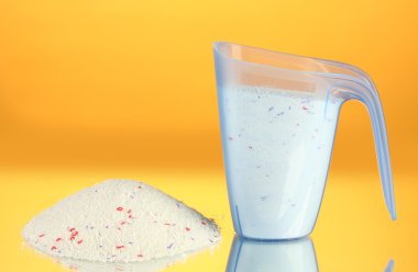 washing powder in a measuring cup, on yellow background close-up clipart