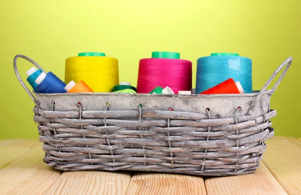 Bright threads in basket on wooden table on green background — Stock Photo, Image