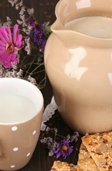 Krug und Tasse Milch mit Keksen auf Holztisch in Großaufnahme — Stockfoto