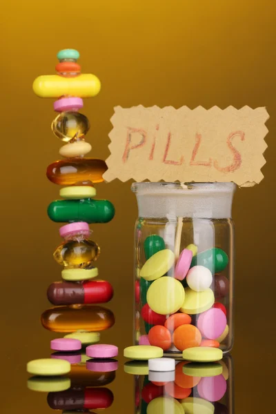 Capsules and pills hill and in receptacle on yellow background — Stock Photo, Image