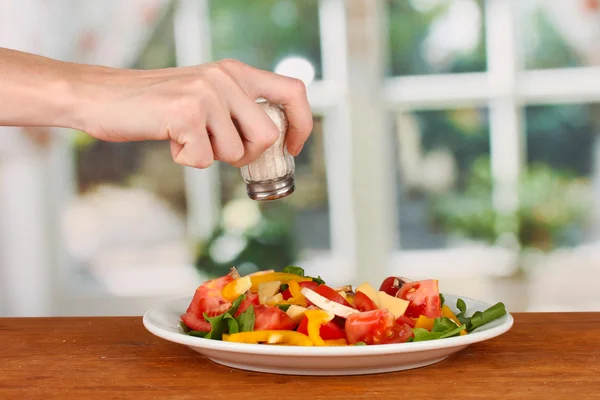 Hand adding salt using salt shaker on bright background — Stock Photo, Image