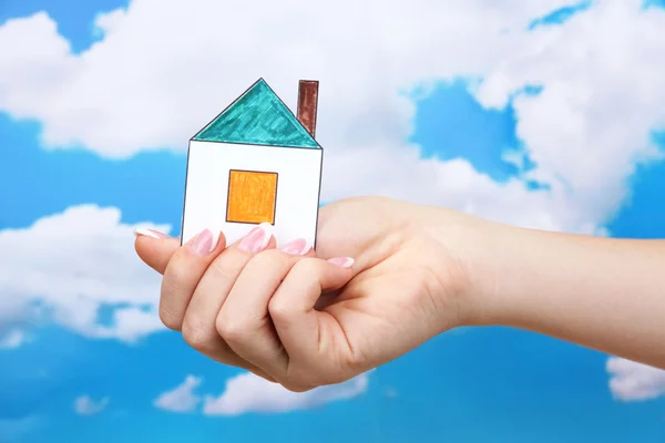 Koncept: kvinna hand med papper hus på himmel bakgrund, närbild — Stockfoto