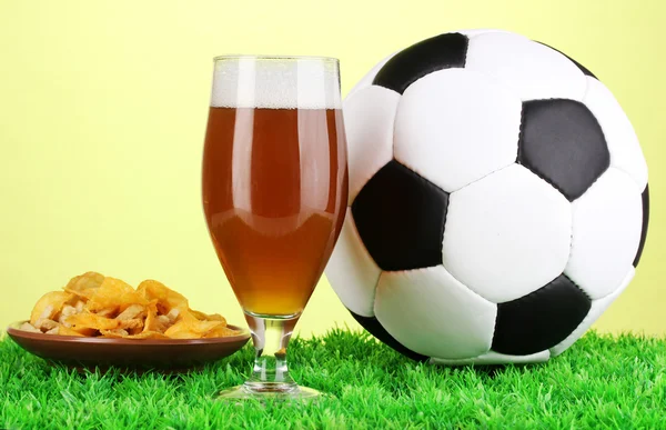 Copo de cerveja com bola de futebol na grama no fundo verde — Fotografia de Stock