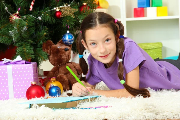 Menina escrevendo carta para o Papai Noel perto da árvore de Natal — Fotografia de Stock