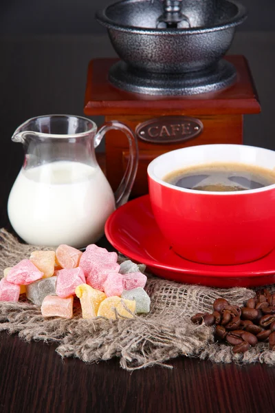 Červené šálek kávy s potěšením rahat, mléka a mlýnek na dřevěný stůl — Stock fotografie
