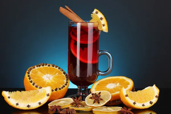 Fragrant mulled wine in glass with spices and oranges around on blue background — Stock Photo, Image