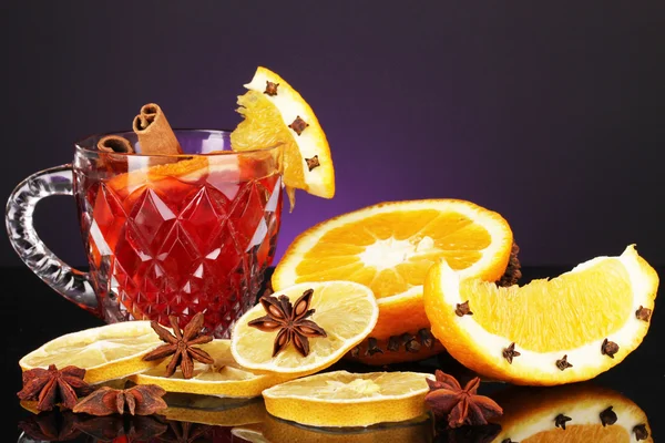 Fragrant mulled wine in glass with spices and oranges around on purple background — Stock Photo, Image